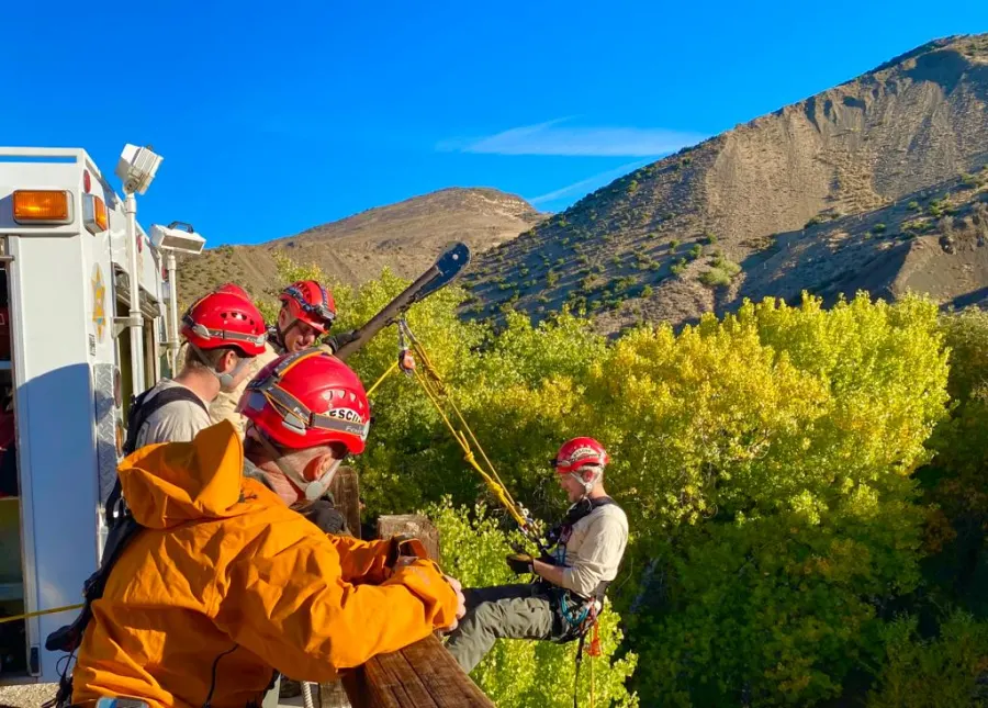 Rescuers in helmets running a rope system beside a rescue truck in a canyon