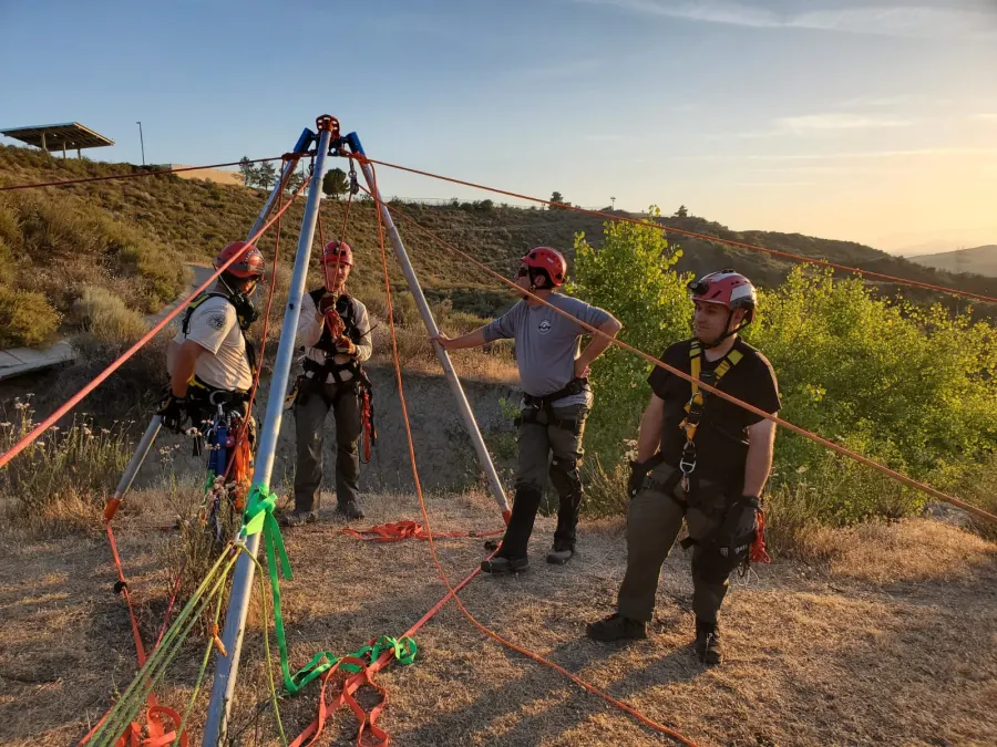 Team members beside a rope rescue tripod at sunset